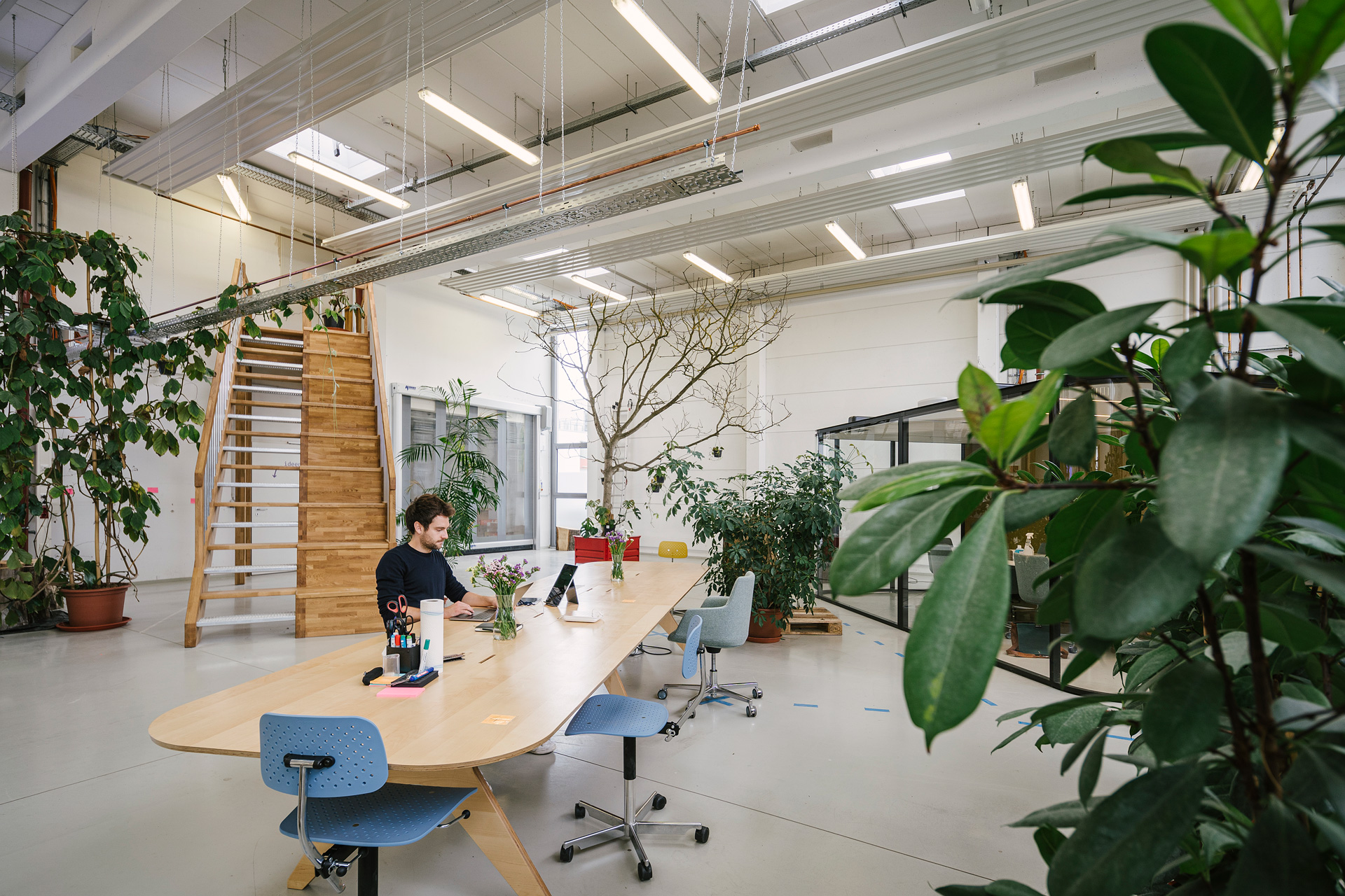 Einblick in den Coworkingspace der Präsenzstelle Luckenwalde mit großem hallenartigen Raum, einem langen Besprechungstisch und am Laptop arbeitender Person